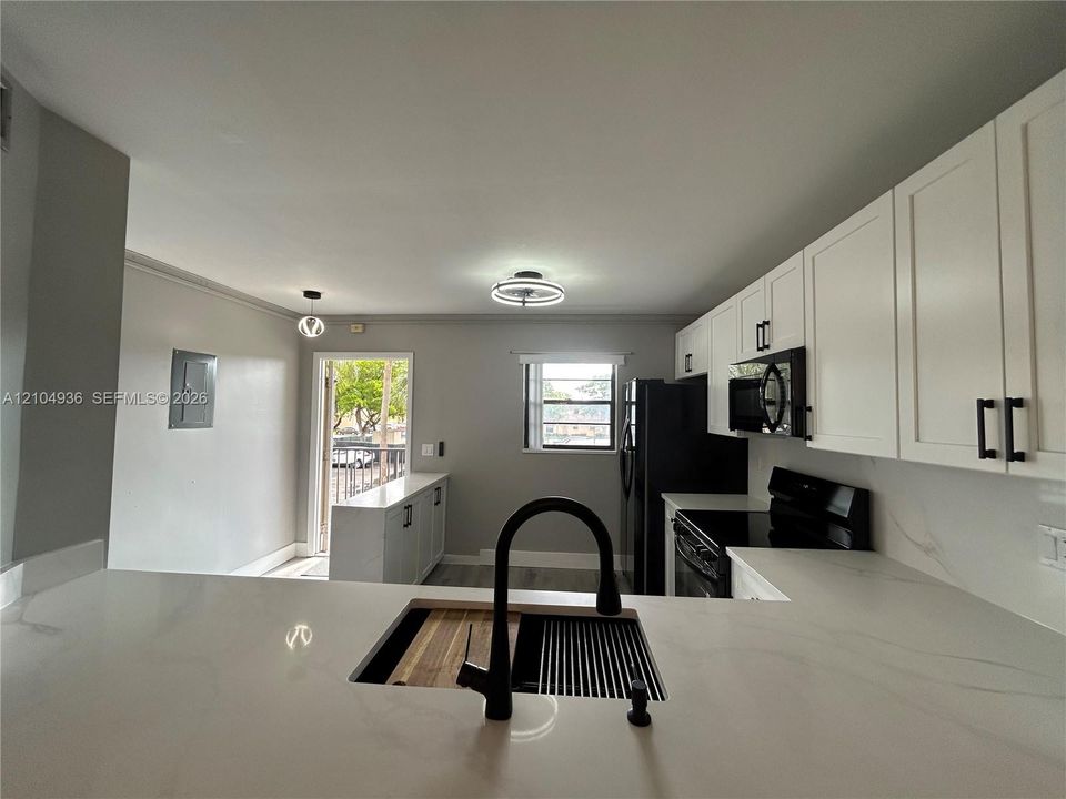Kitchen featuring white shaker-style cabinetry, quartz countertops, a matte black high-arc faucet, and an undermount workstation sink