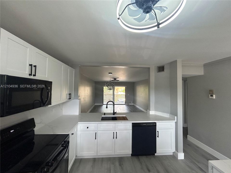 Kitchen featuring white shaker-style cabinetry, white countertops, black built-in appliances, a matte black kitchen faucet, and wood-finish flooring