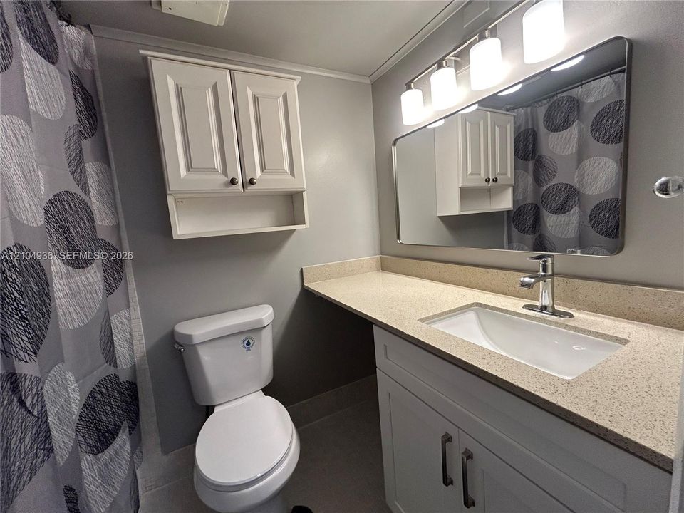 Bathroom featuring a white vanity with a neutral solid-surface countertop, an integrated rectangular sink, wall-mounted cabinetry, a large rectangular mirror, and a four-light fixture