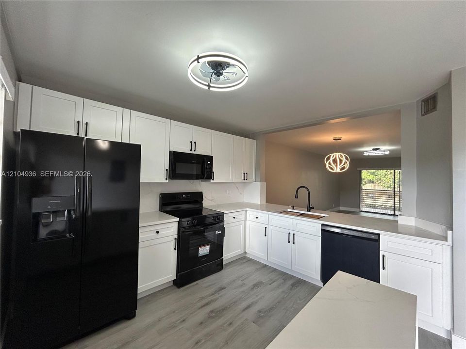 Kitchen featuring white shaker-style cabinetry, quartz countertops, wood-finish flooring, a matte black faucet, and a black appliance package
