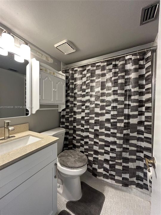 Bathroom featuring a vanity with a light-tone countertop, an integrated rectangular sink, wall-mounted cabinetry, and a shower-tub combination