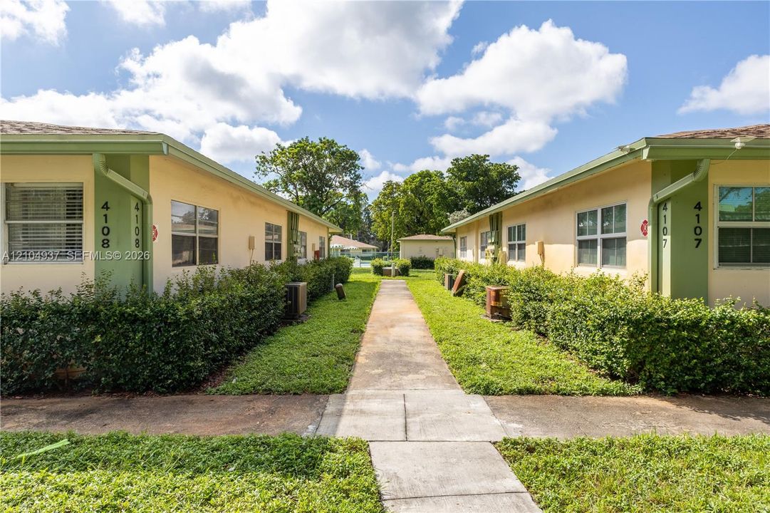 Exterior view of stucco buildings featuring a concrete walkway, trimmed shrubbery, and multi-pane horizontal windows