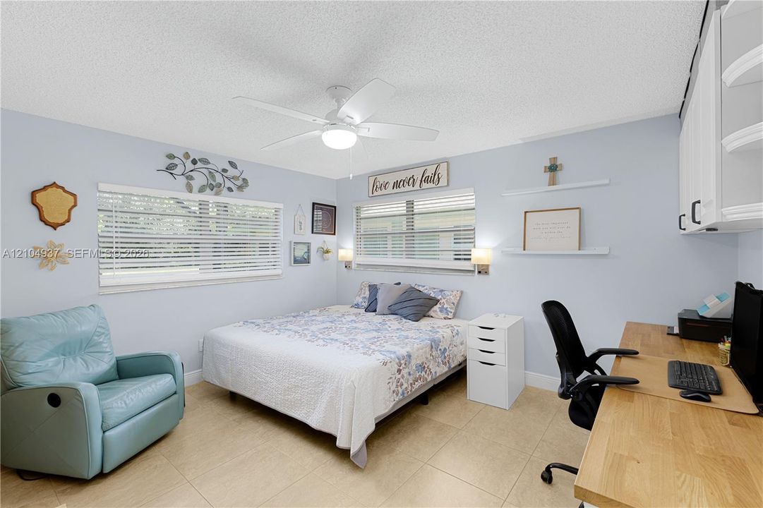Neutral-toned tile flooring, dual windows with horizontal blinds, built-in upper cabinetry, and a ceiling fan with integrated lighting