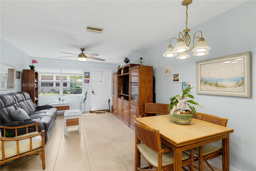 Neutral-tone tile flooring, multi-pane windows, ceiling fan, and ornate five-light chandelier