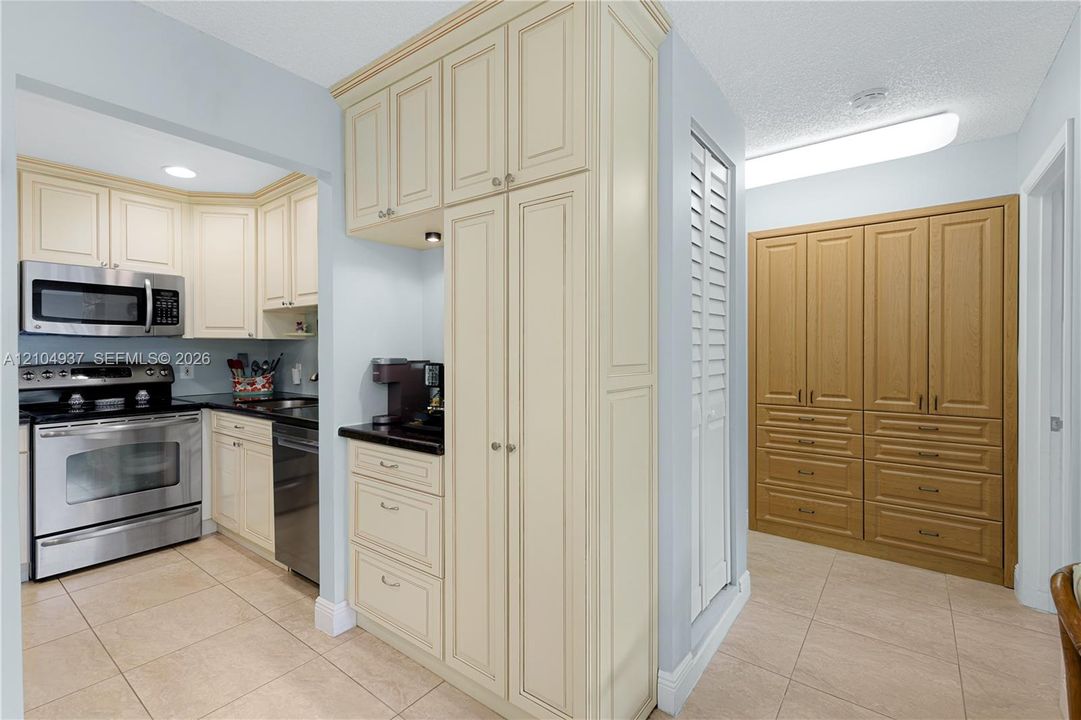 Kitchen featuring cream-colored cabinetry, stainless steel appliances, dark stone-finish countertops, tile flooring, and integrated wood-tone storage cabinetry
