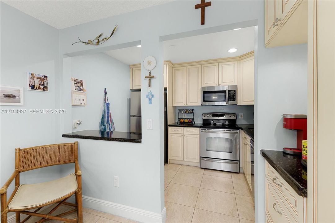 Kitchen featuring off-white cabinetry, dark stone countertops, stainless steel appliances, and ceramic tile flooring