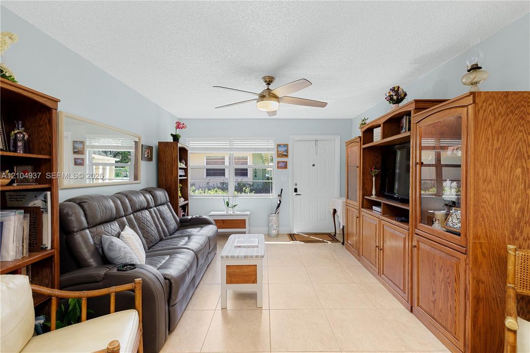 Living area featuring large-format tile flooring, a central ceiling fan with integrated lighting, expansive multi-pane windows, and a built-in wooden media cabinet
