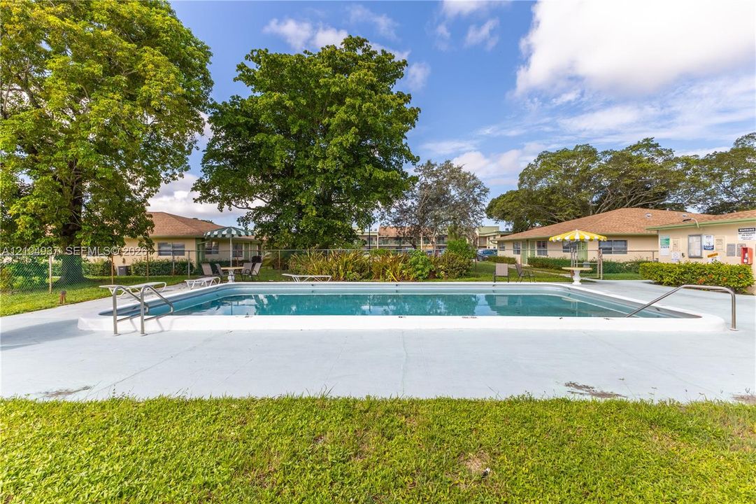 Rectangular in-ground swimming pool featuring a concrete pool deck, stainless steel entry rails, chain-link perimeter fencing, and mature landscaping