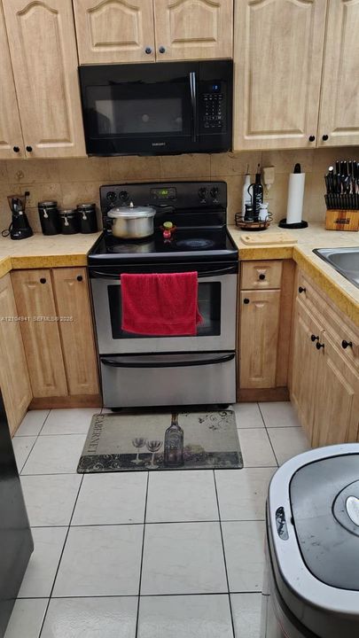 Kitchen featuring light-finish cabinetry, tile countertops, tile flooring, and stainless steel range and microwave