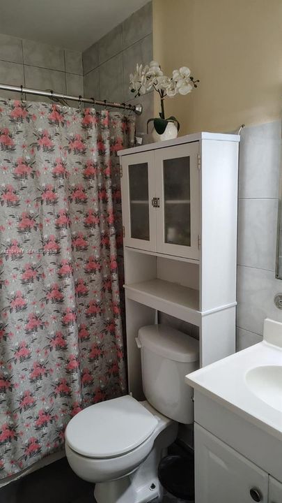 Bathroom featuring a white vanity cabinet, ceramic tile walls, and a shower area with a metal tension rod