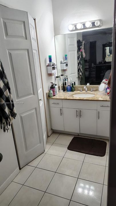 Bathroom vanity featuring a stone countertop, an integrated oval sink, white cabinetry with metal hardware, a wall-to-wall mirror, and a four-bulb vanity light fixture