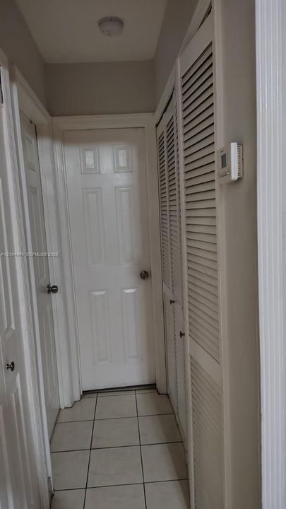 Interior hallway featuring white six-panel doors, louvered closet doors, and ceramic tile flooring