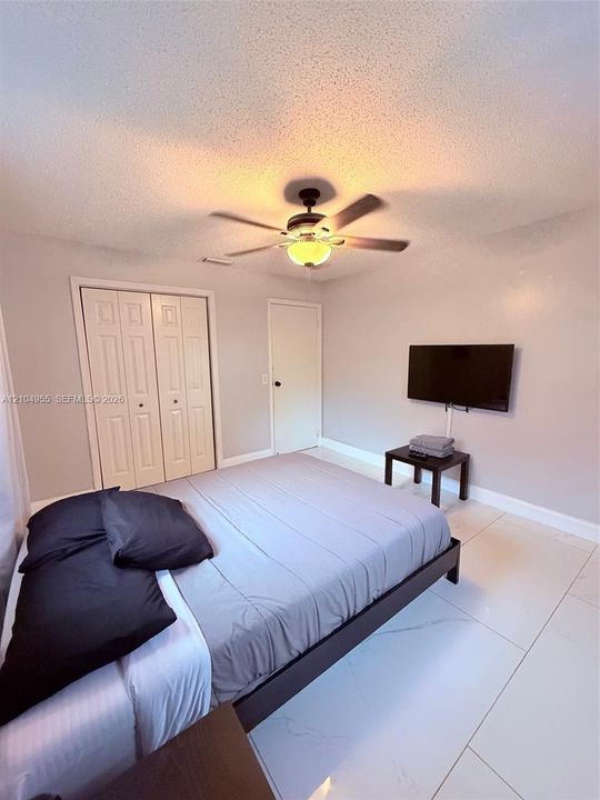 Large-format tile flooring, ceiling fan with integrated lighting, and bi-fold closet doors