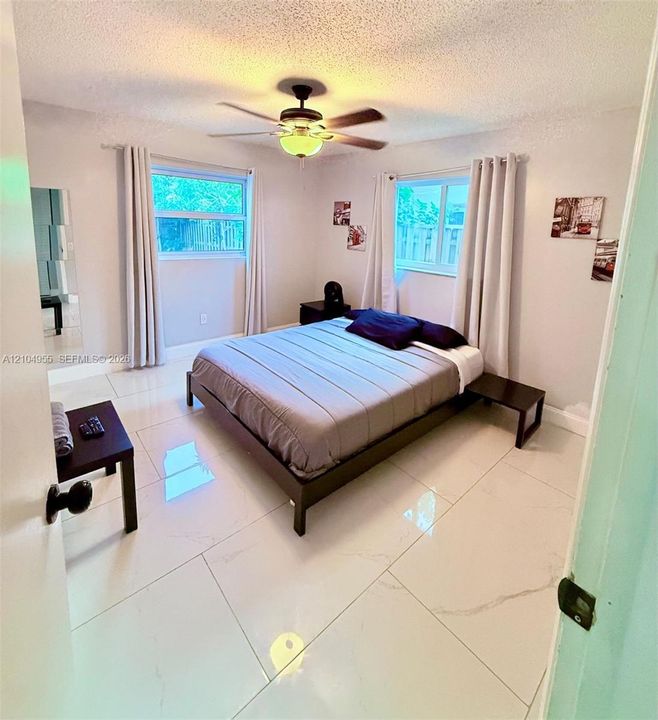 Large-format polished tile flooring, ceiling fan with integrated lighting, and dual windows