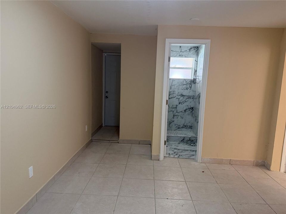 Tiled flooring throughout, neutral wall finishes, and a contemporary shower enclosure with marble-patterned wall panels