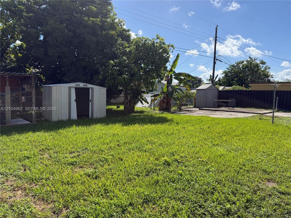 Expansive grassy yard area featuring mature trees, a metal storage shed, and a concrete patio