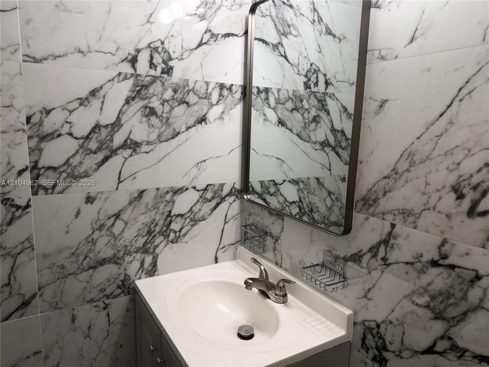Full-height wall tiling with a marble-effect finish, a vanity with an integrated sink, and a framed mirror