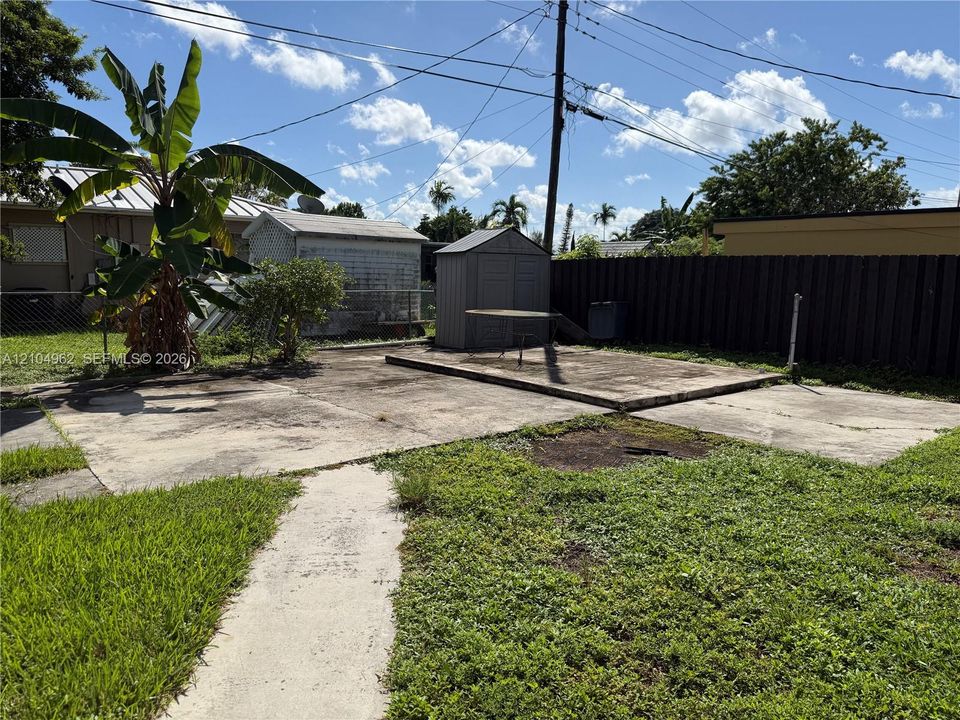 Spacious backyard with concrete patio areas, two storage sheds, and a wooden privacy fence