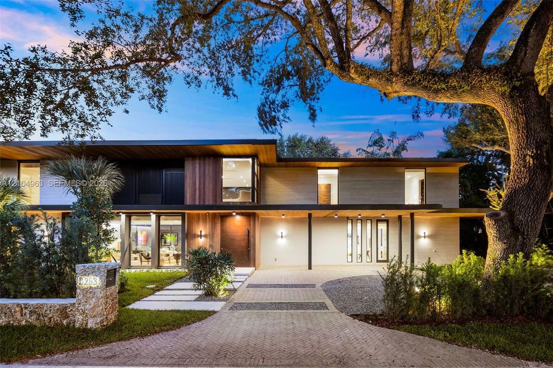 Modern multi-level exterior featuring wood-paneled siding, stone-finished masonry, expansive floor-to-ceiling glass windows, and a paved herringbone driveway