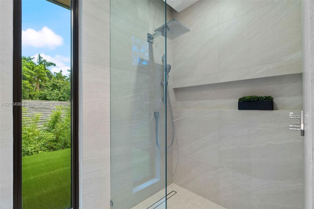 Walk-in shower featuring floor-to-ceiling stone-finish tile, frameless glass enclosure, rainfall shower head, handheld sprayer, and an integrated recessed storage niche