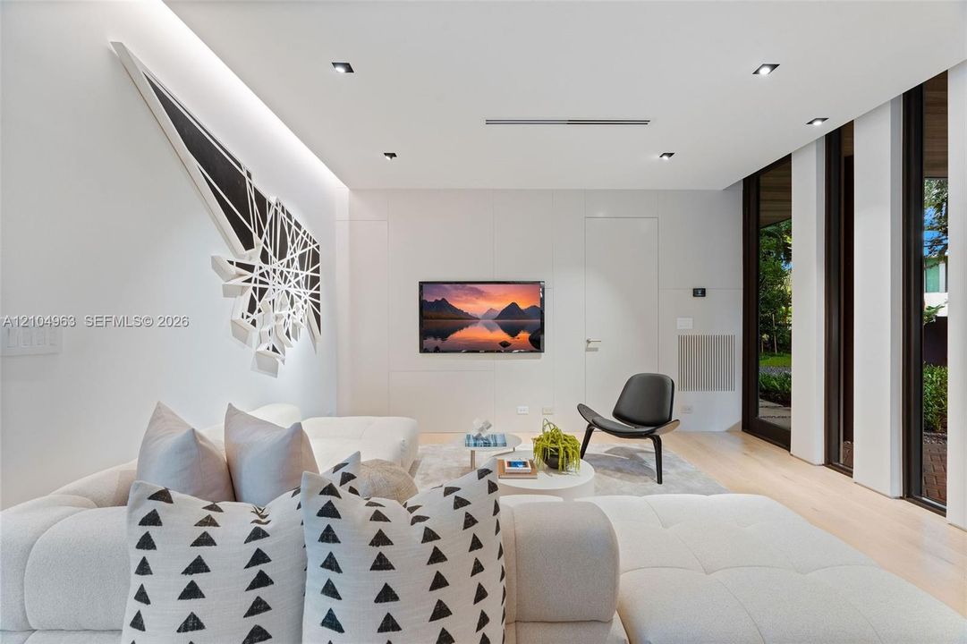 Contemporary interior featuring smooth wall panels, light-toned wood-finish flooring, recessed ceiling lighting, and floor-to-ceiling windows with dark frames
