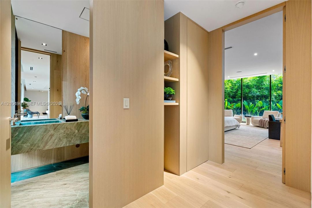 Custom light-toned wood cabinetry with integrated shelving, stone vanity with a rectangular sink, full-height wall mirrors, and wood-finish flooring