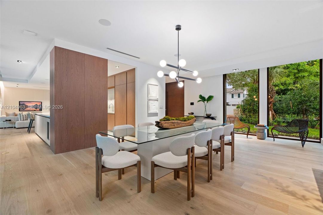Dining area featuring wood-finish flooring, floor-to-ceiling windows, a modern multi-light spherical chandelier, and floor-to-ceiling wood-panel accent wall