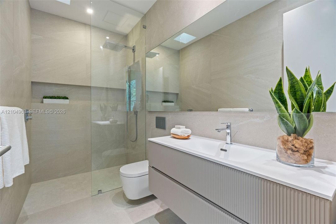 Modern bathroom featuring a textured floating vanity, integrated rectangular sink, wall-to-wall mirror, glass-enclosed walk-in shower with a rain-style showerhead, and neutral-toned wall tiles