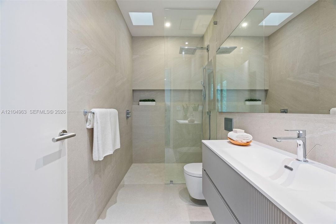 Modern bathroom featuring floor-to-ceiling textured wall tiling, a floating vanity with a seamless integrated sink, a glass-enclosed shower with a built-in recessed wall niche, and a large wall-to-wall mirror