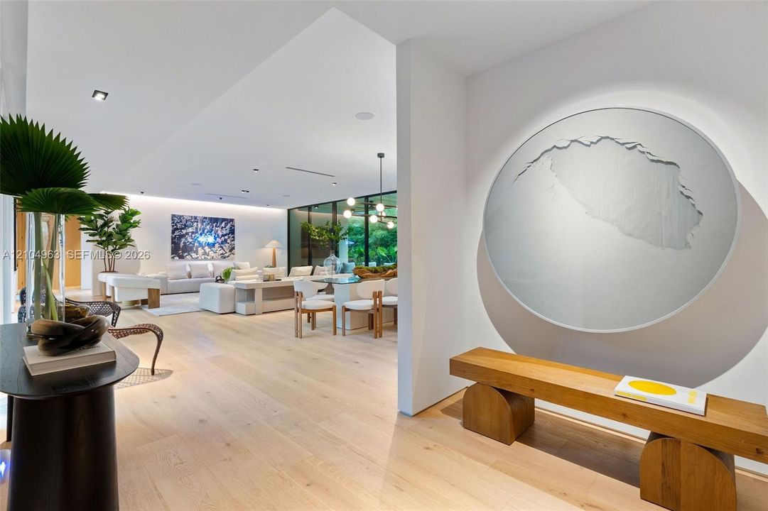 Open-concept interior featuring light wood-finish flooring, recessed ceiling lighting, wall-mounted accent lighting, and expansive floor-to-ceiling glass panels