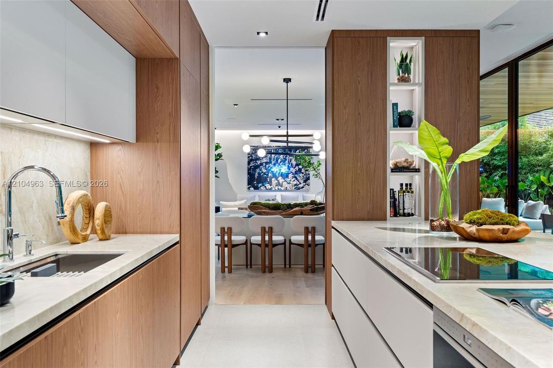 Modern kitchen featuring flat-panel wood cabinetry, quartz countertops, a high-arc chrome faucet, integrated shelving, and a smooth cooktop