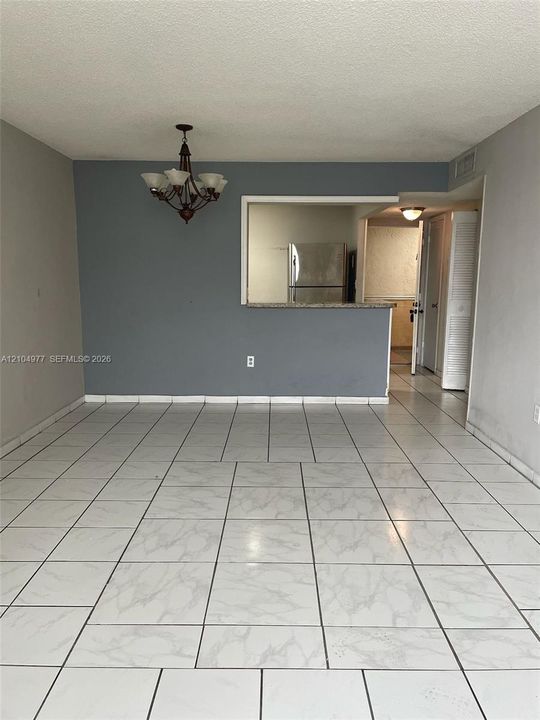 Living area featuring light-toned tile flooring, a decorative chandelier, and a cutout pass-through window with a stone-surface breakfast bar