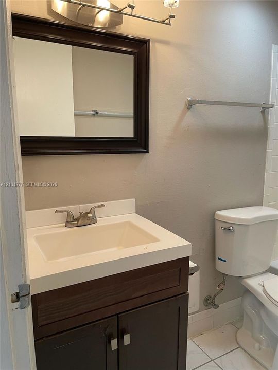 Dark wood-finish vanity with an integrated countertop sink, metal dual-handle faucet, framed wall mirror, and ceramic tile flooring