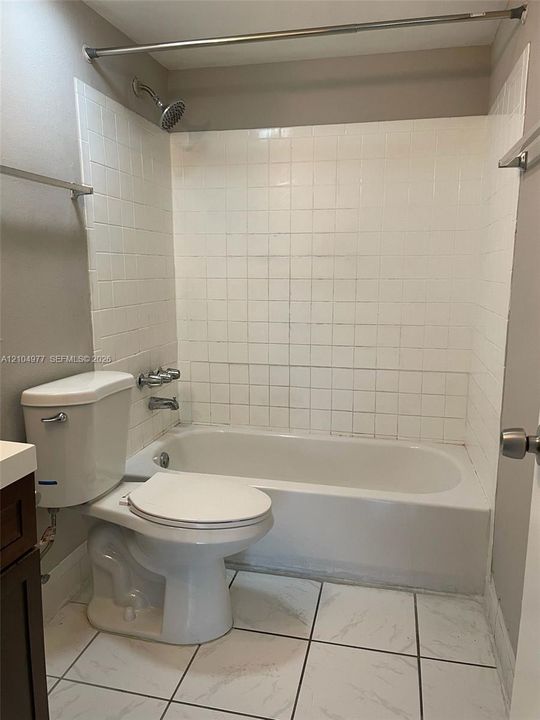 Bathtub with a white tile surround, integrated shower fixture, dual-handle faucet, and white stone-patterned tile flooring