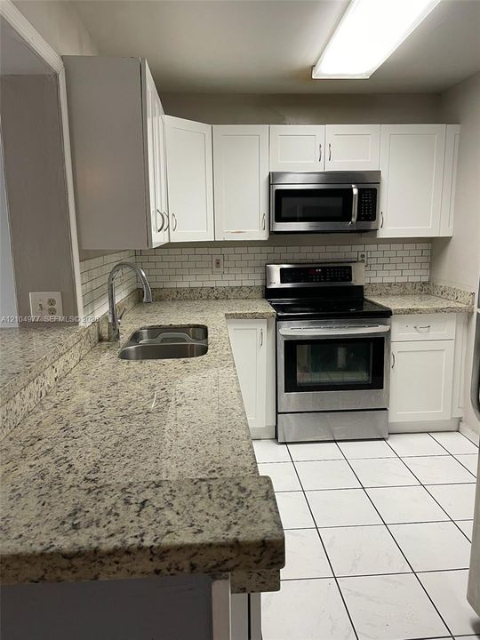 Kitchen featuring white cabinetry, stone-finish countertops, stainless steel appliances, subway tile backsplash, and ceramic floor tiling