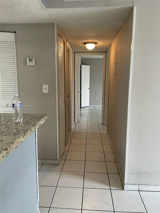 Hallway featuring tile flooring, neutral wall paint, dual louvered-door closets, and a flush-mount ceiling light fixture
