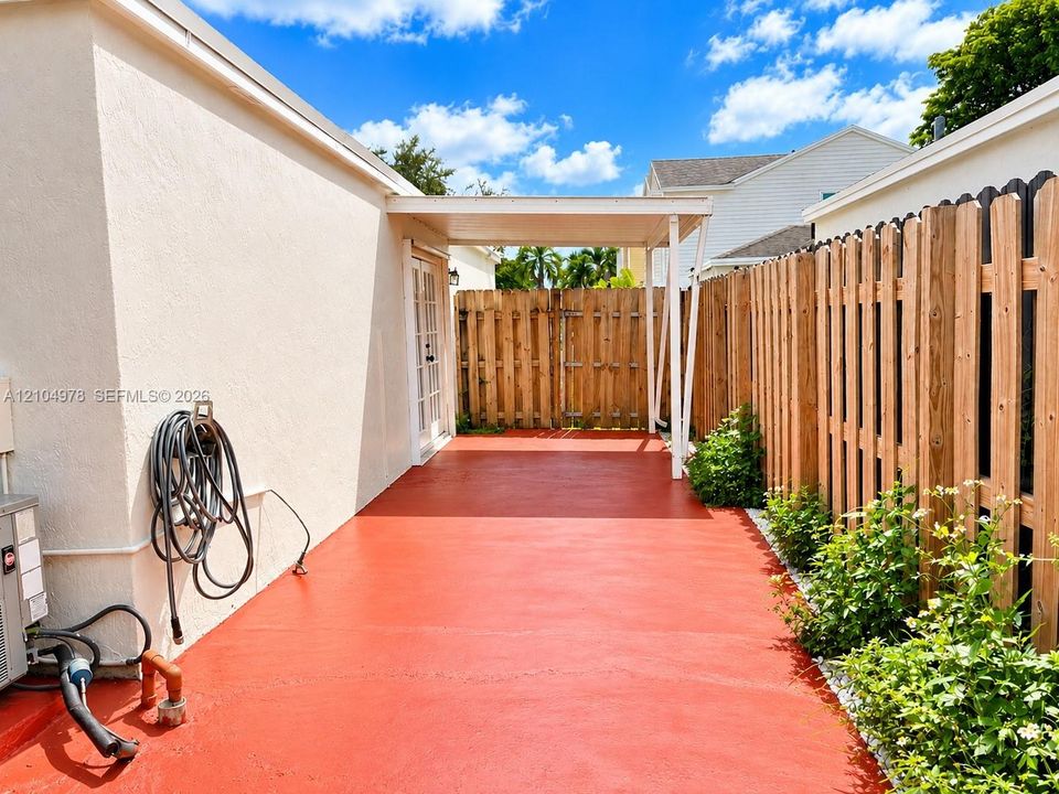 Expansive red-painted concrete patio with a white stucco exterior, covered awning, and wooden privacy fencing