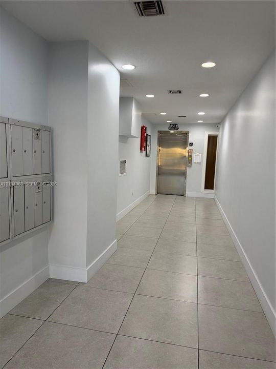 Hallway featuring large-format ceramic tile flooring, recessed ceiling lighting, a stainless steel elevator, and wall-mounted metal mailboxes