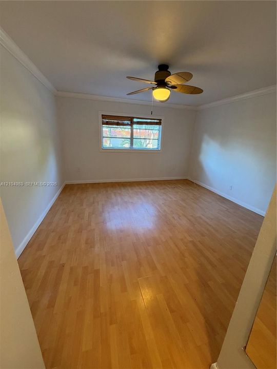 Interior space featuring wood-finish flooring, neutral wall paint, crown molding, and a multi-blade ceiling fan with a central light fixture