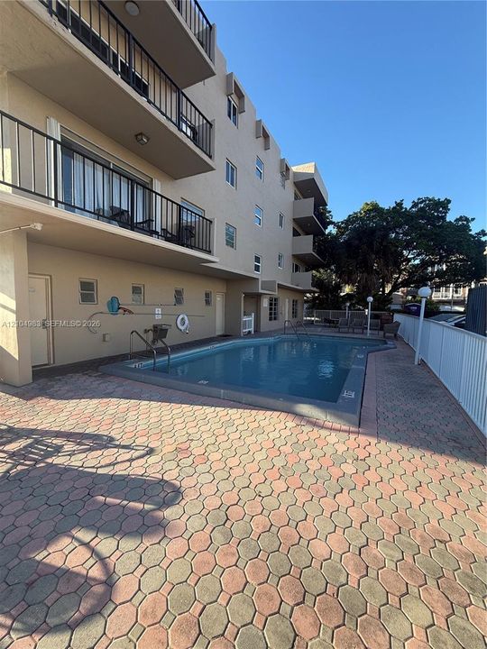 In-ground swimming pool featuring a concrete deck with paver-style surfacing and metal perimeter fencing