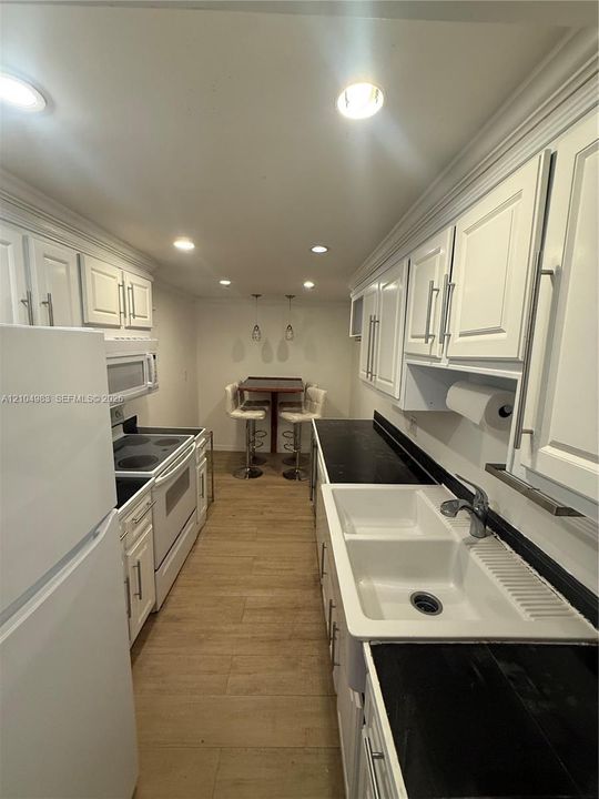 Kitchen featuring white shaker-style cabinetry, dark stone-finish countertops, apron-front farmhouse sink with pull-down faucet, recessed lighting, and wood-finish flooring