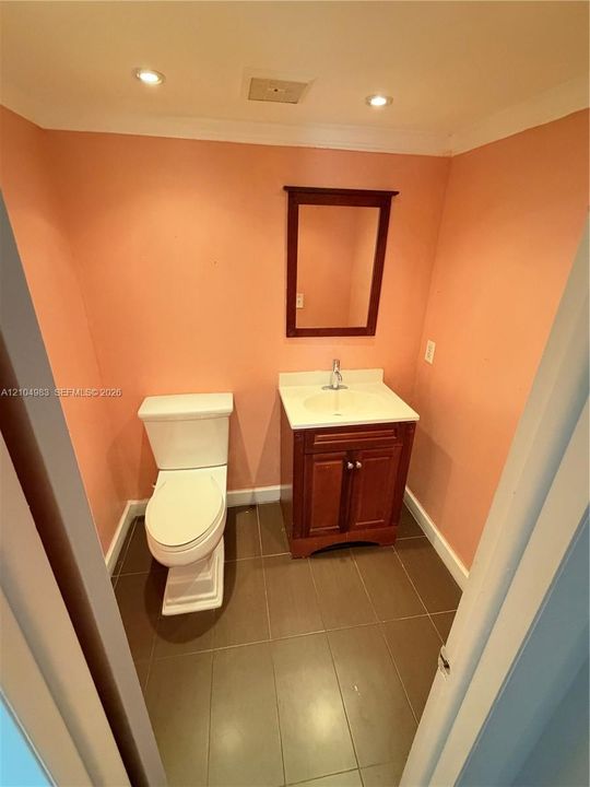 Wood-finish vanity with a rectangular sink, white countertop, recessed lighting, and tile flooring