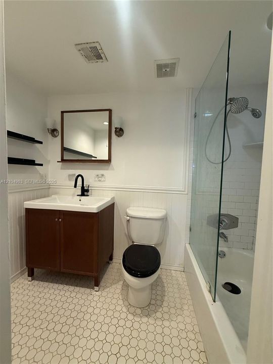 Bathroom featuring a vanity with an integrated basin, matte black faucet, frameless glass shower enclosure, subway tile shower surround, and hexagonal tile flooring