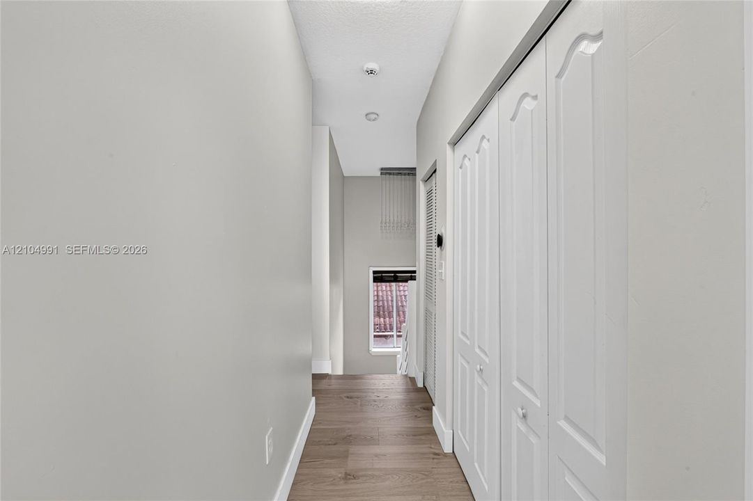 Hallway featuring wood-finish flooring, white paneled closet doors, and recessed ceiling lighting