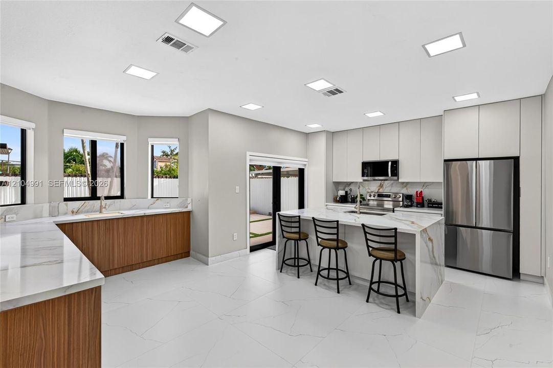 Modern kitchen featuring flat-panel cabinetry, stone-finish countertops with waterfall edge, stainless steel appliances, and large-format tile flooring