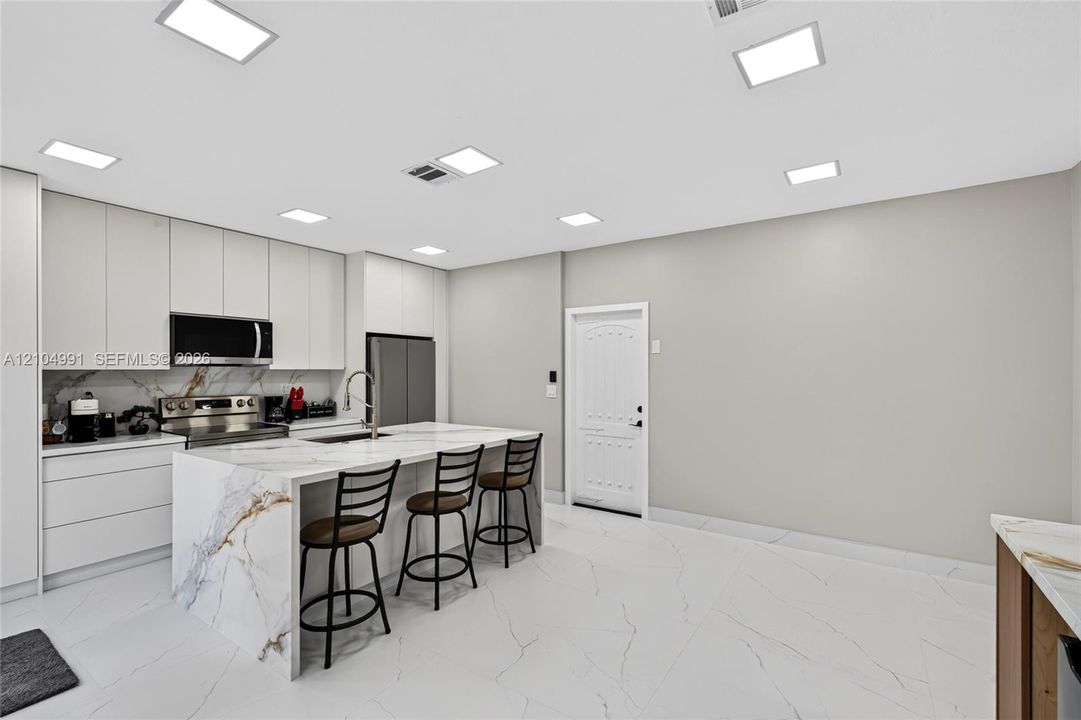 Kitchen featuring floor-to-ceiling cabinetry, a waterfall-edge island with stone-finish countertops, large-format tile flooring, and integrated square LED ceiling lighting