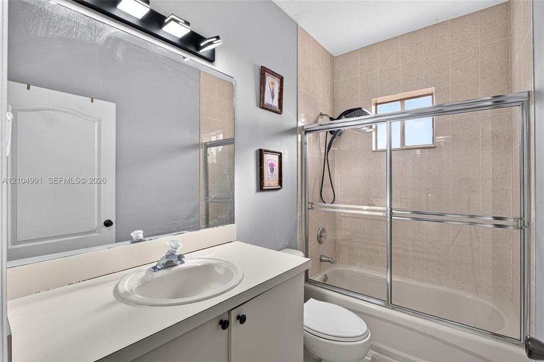 Bathroom featuring a vanity with a white countertop and oval basin, wall-mounted vanity lighting, a full-width mirror, and a tub-shower combination with a sliding glass door and tiled surround