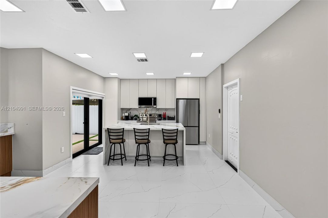 Kitchen featuring floor-to-ceiling cabinetry, a central island with a stone-surface countertop, stainless steel appliances, and large-format tile flooring with recessed lighting