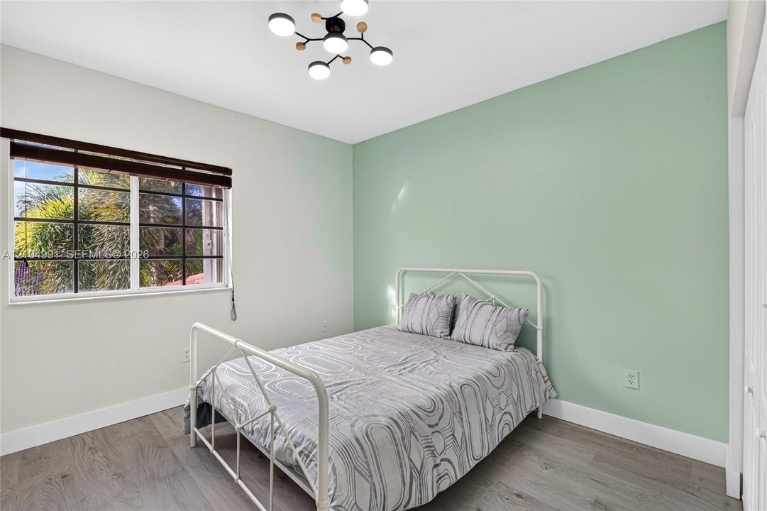 Room featuring wood-finish flooring, a contemporary multi-light fixture, an accent wall, and a multi-pane window with a horizontal blind