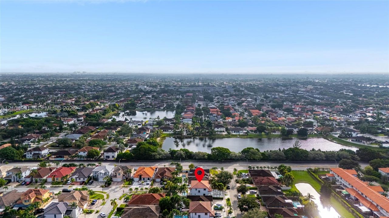 Aerial perspective of a multi-story residence with a pitched tile roof, situated in a suburban setting featuring nearby ponds and mature canopy trees